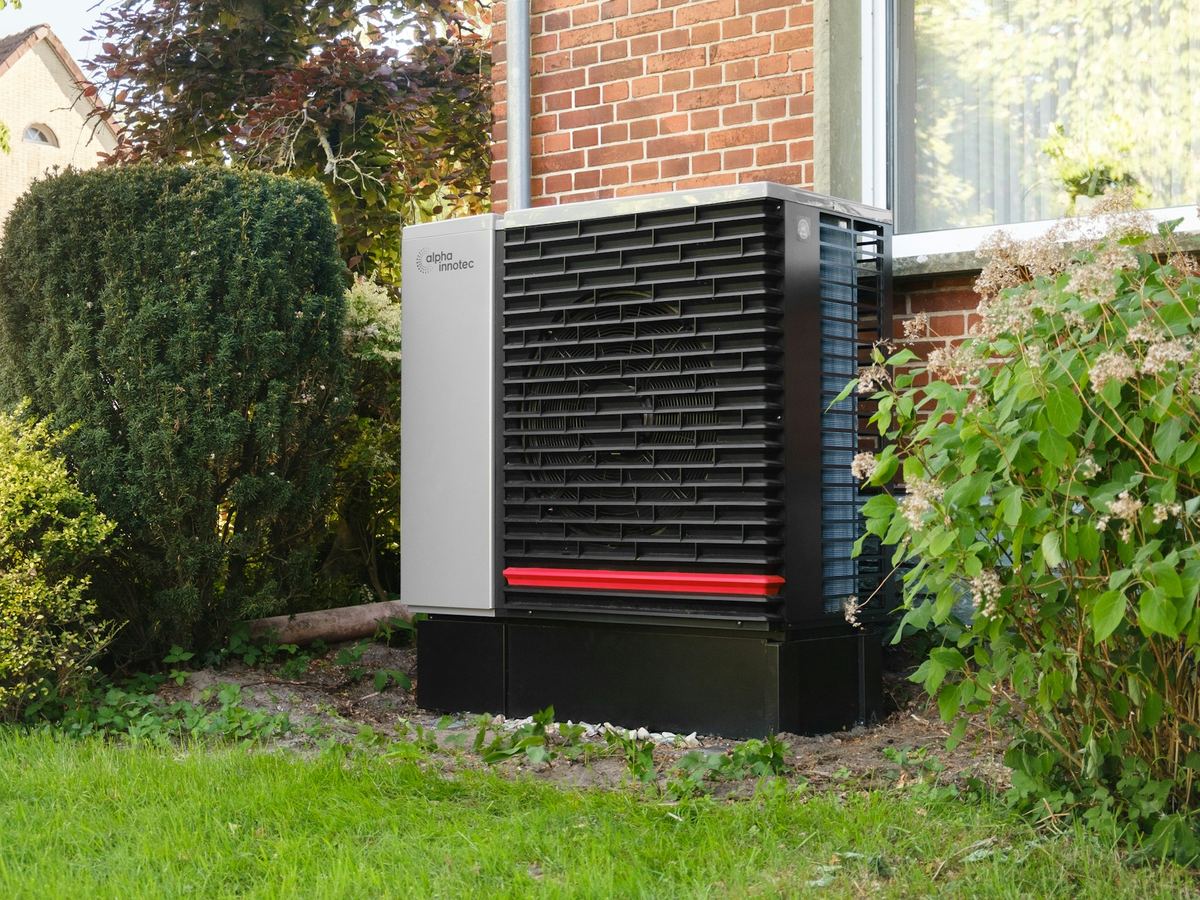Outdoor heat pump next to a brick home with a landscaped garden