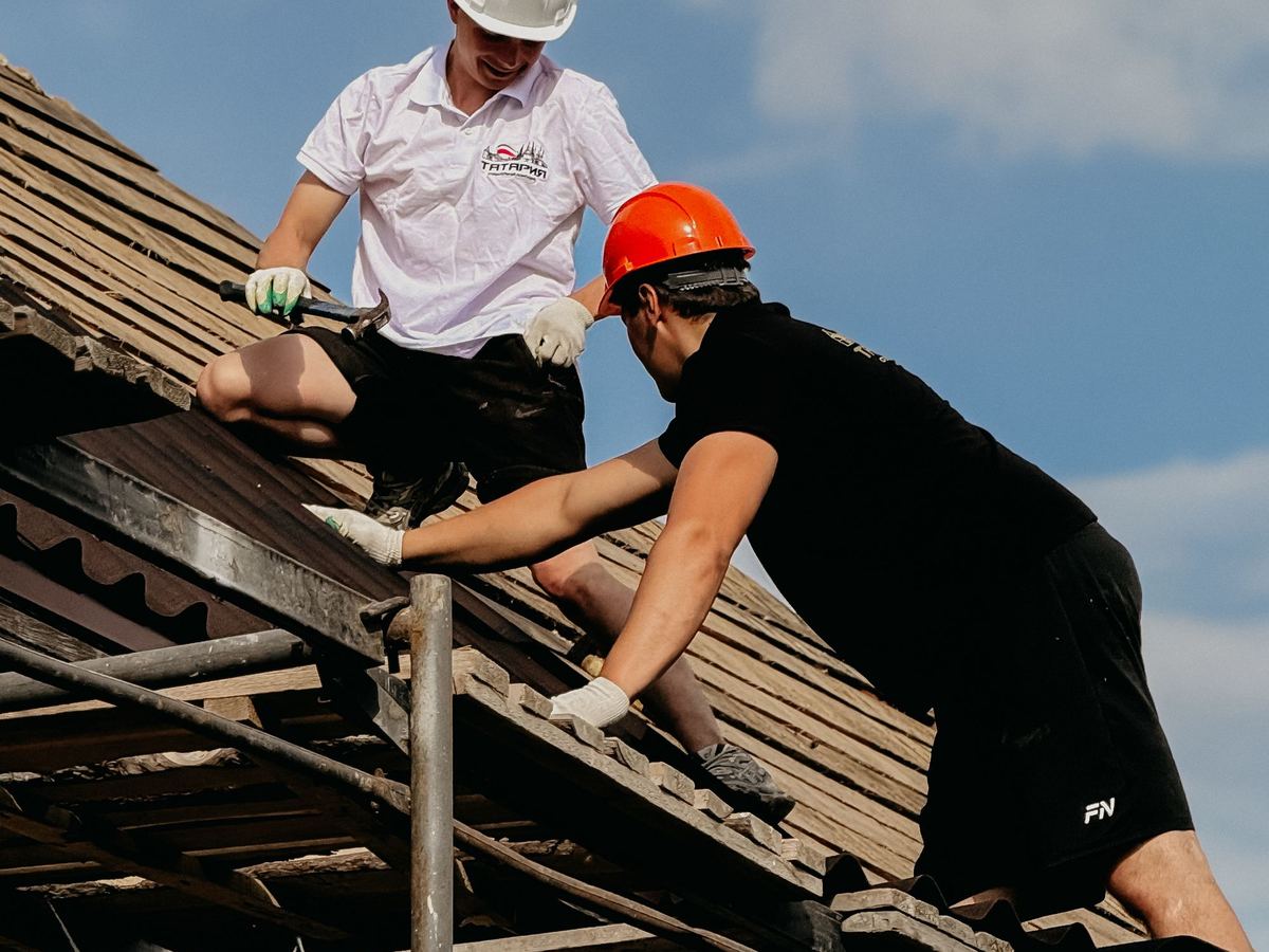Two roofers in hard hats repairing a damaged roof
