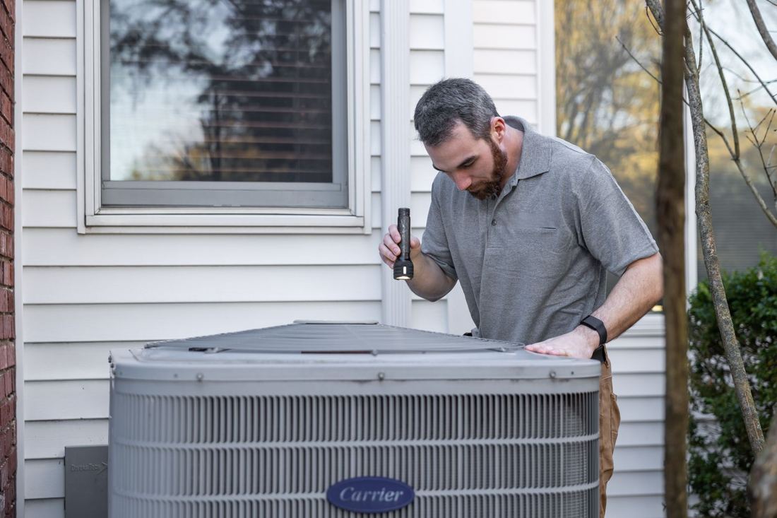HVAC technician checking an outdoor air conditioner condenser beside a home